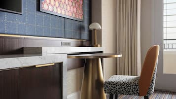 A modern hotel room with a marble countertop, a gold lamp, a patterned chair, and a large window with curtains.