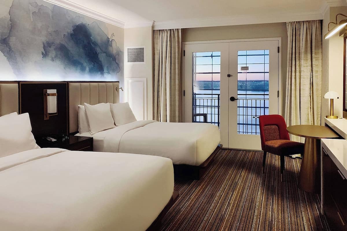 Een hotelkamer met twee bedden, een bureau, een stoel, een groot raam met uitzicht en een modern abstract schilderij aan de muur.