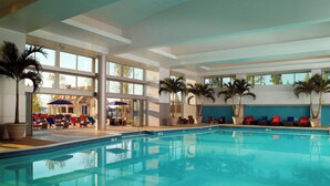 Une piscine intérieure à l’eau d’un bleu cristallin, entourée de chaises longues et de palmiers.
