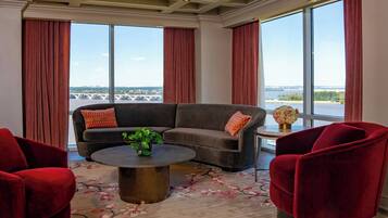 A modern living room with a sofa, red chairs, a coffee table, and a large window with a view of a bridge and water.
