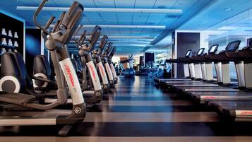 Un gimnasio con varias máquinas de cardio, incluyendo cintas de correr y elípticas, dispuestas en filas.