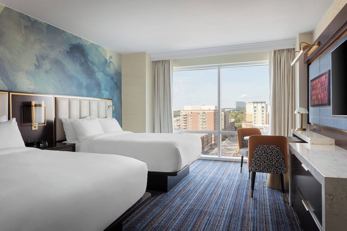 Een hotelkamer met twee bedden, een groot raam met uitzicht op de stad, een flatscreen televisie en een klein tafeltje met een stoel.