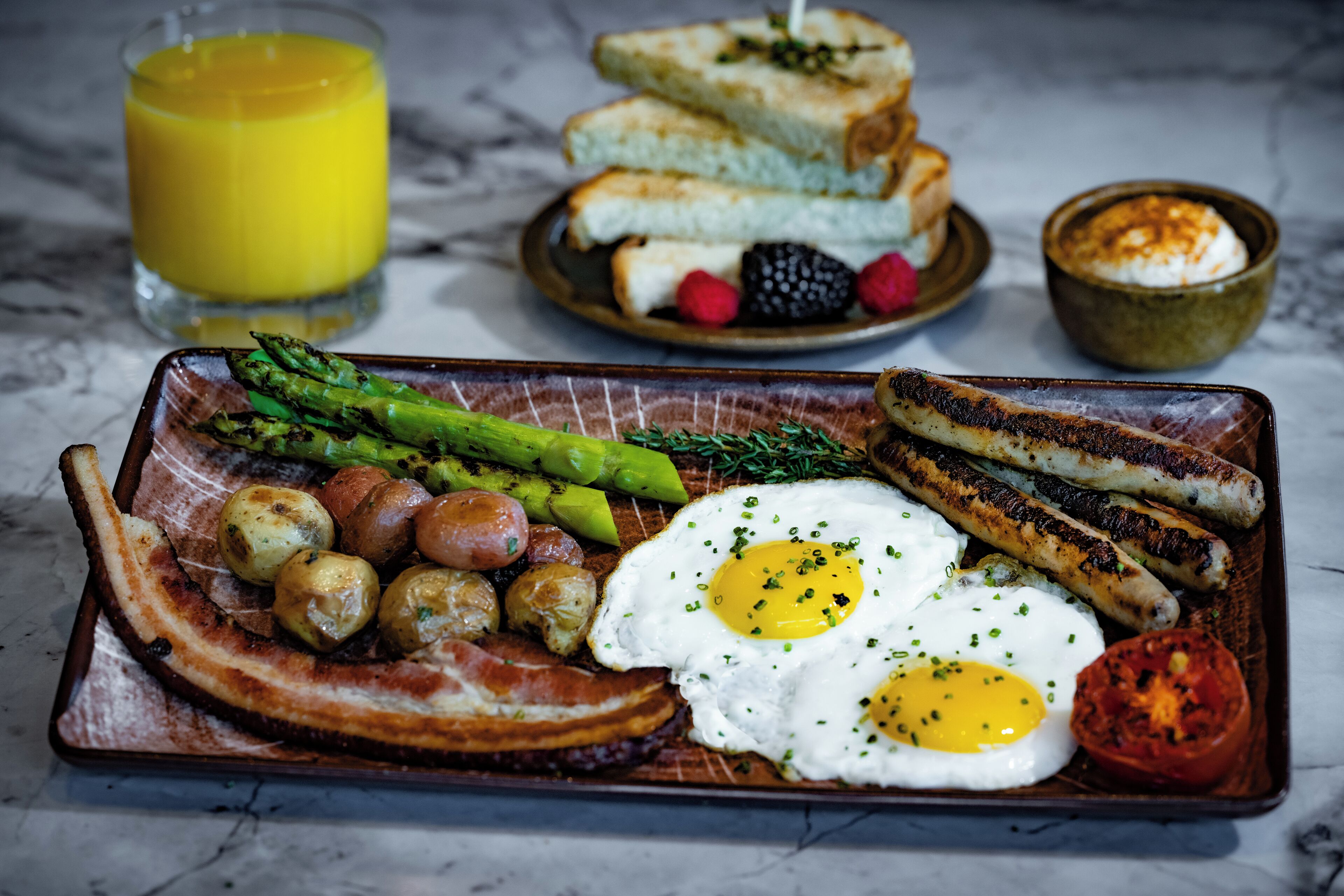 A breakfast plate with eggs, sausages, bacon, asparagus, and toast.