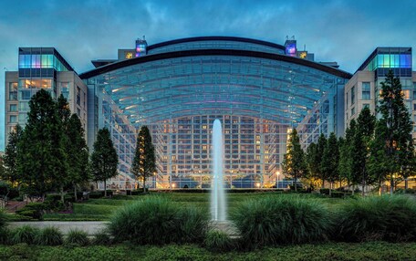 A modern hotel with a glass facade, a central fountain, and a landscaped garden.