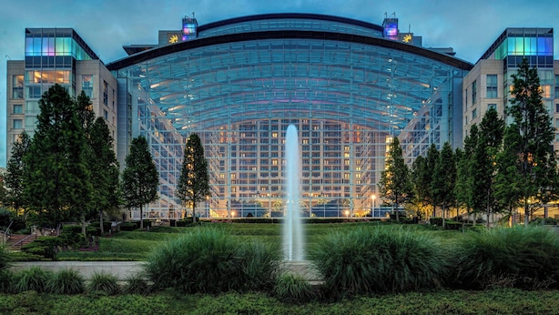 Un hôtel moderne doté d’une façade en verre, d’une fontaine centrale et d’un jardin aménagé.