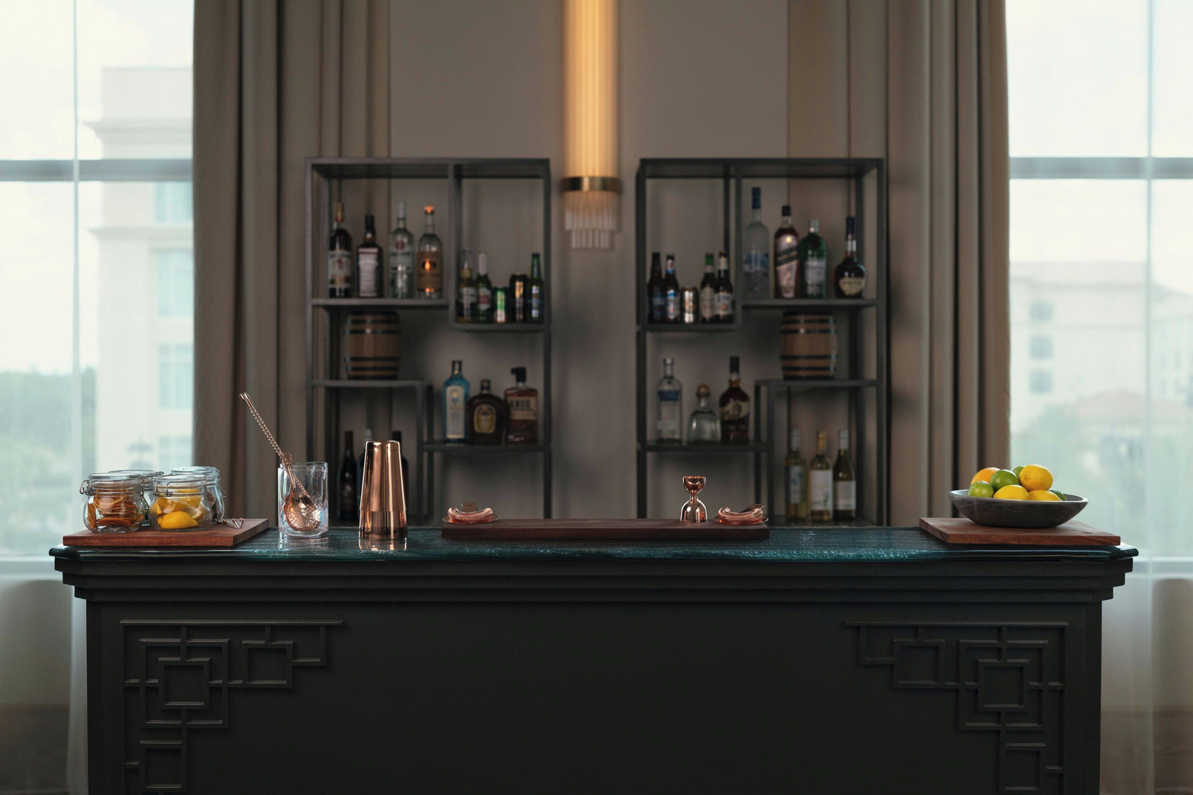 A bar area with shelves of liquor bottles, a bar counter, and a bowl of lemons.