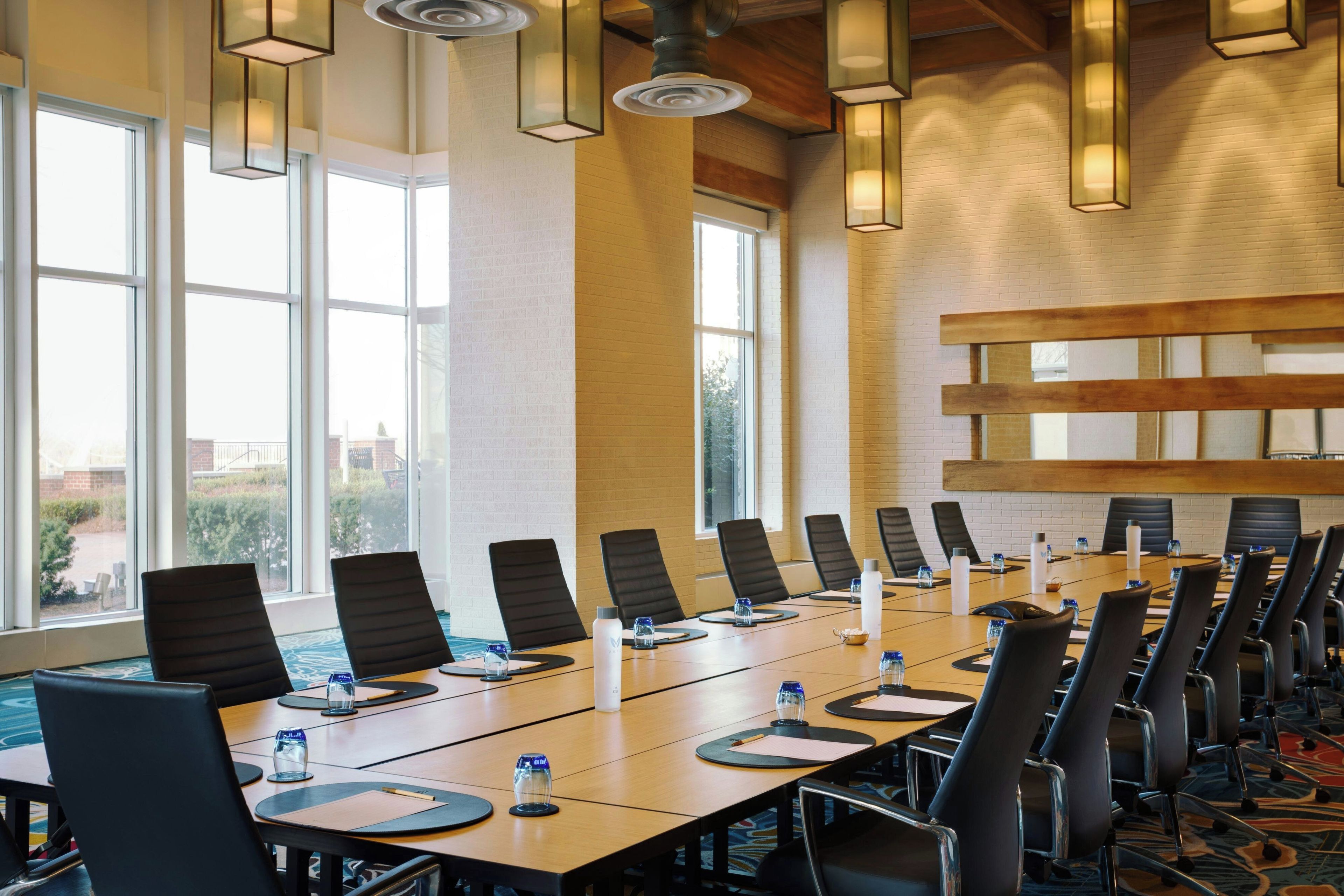 A conference room with a long table, chairs, and a view through large windows.
