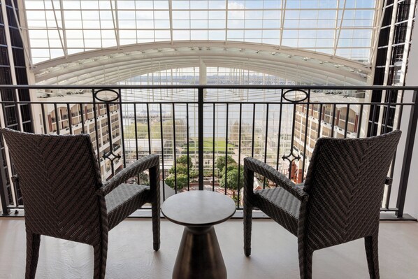A balcony with two wicker chairs and a small table, overlooking a cityscape and a body of water.