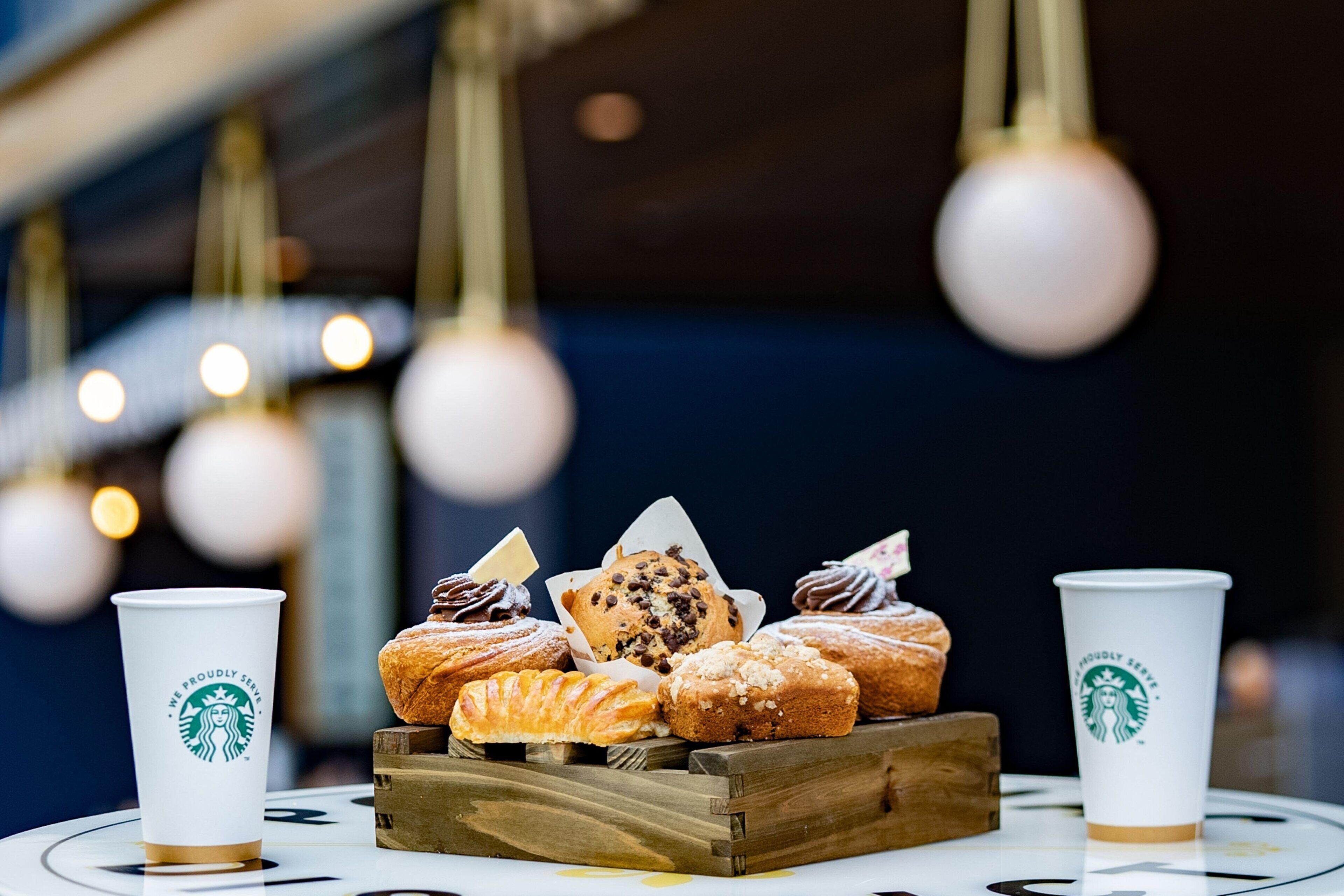 A tray of assorted pastries and two Starbucks cups on a table.