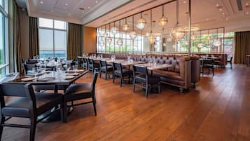 A spacious restaurant with high ceilings, large windows, and modern pendant lighting.