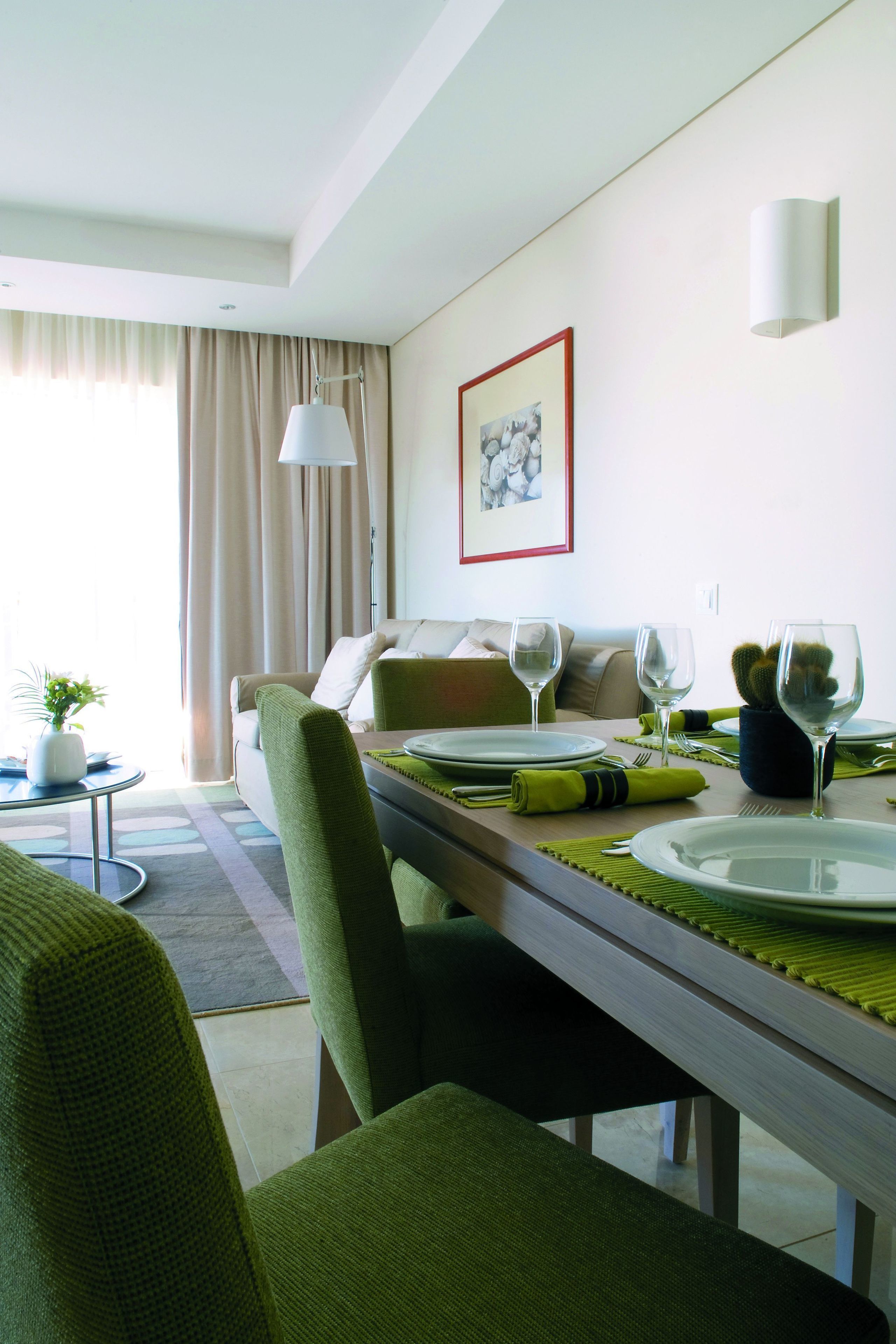 A dining area with a table set for two, a sofa, a lamp, and a framed picture on the wall.