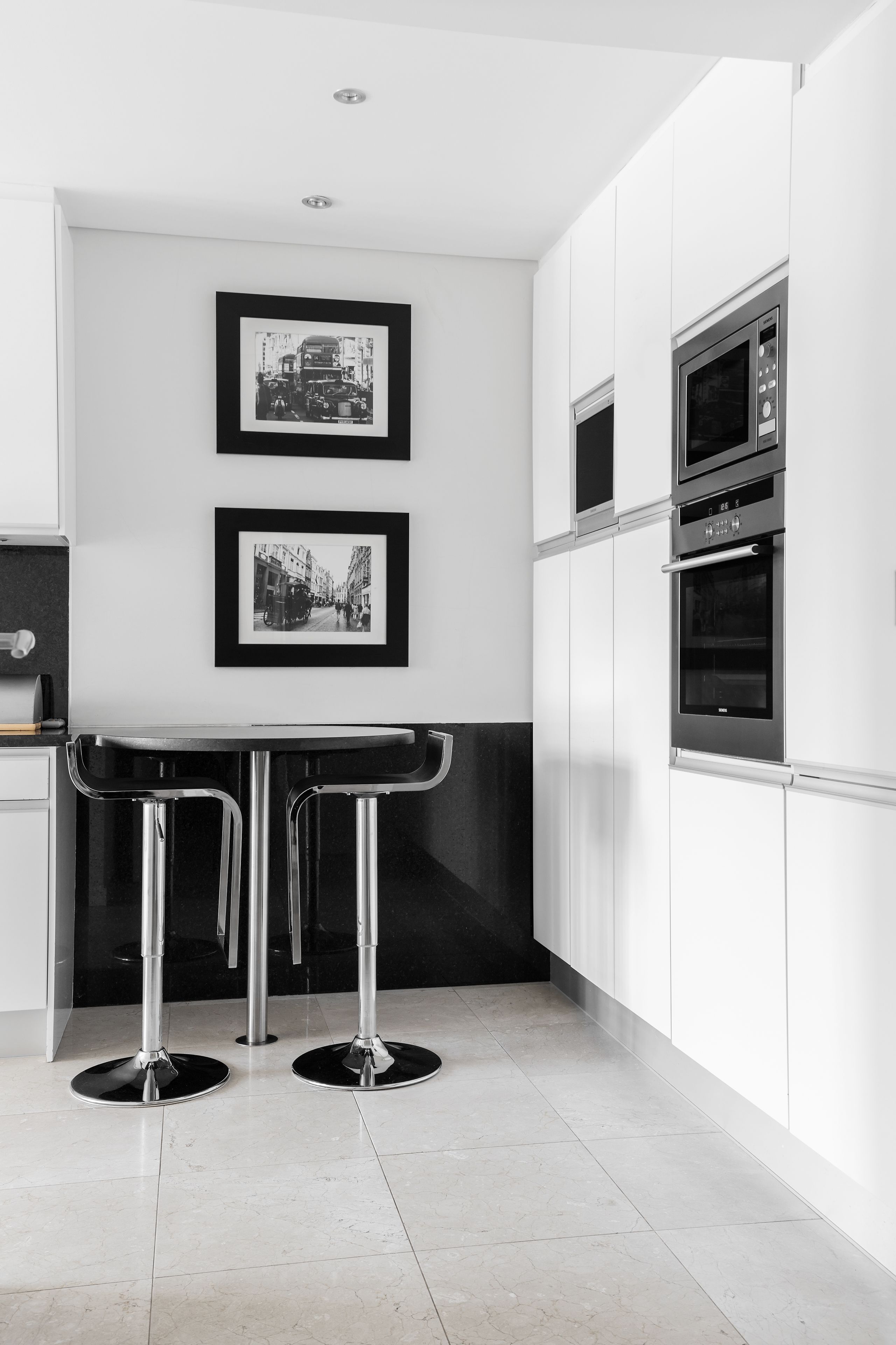 A modern kitchen with white cabinets, stainless steel appliances, and two framed black and white photographs on the wall.