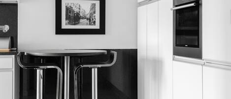 A modern kitchen with white cabinets, stainless steel appliances, and two framed black and white photographs on the wall.
