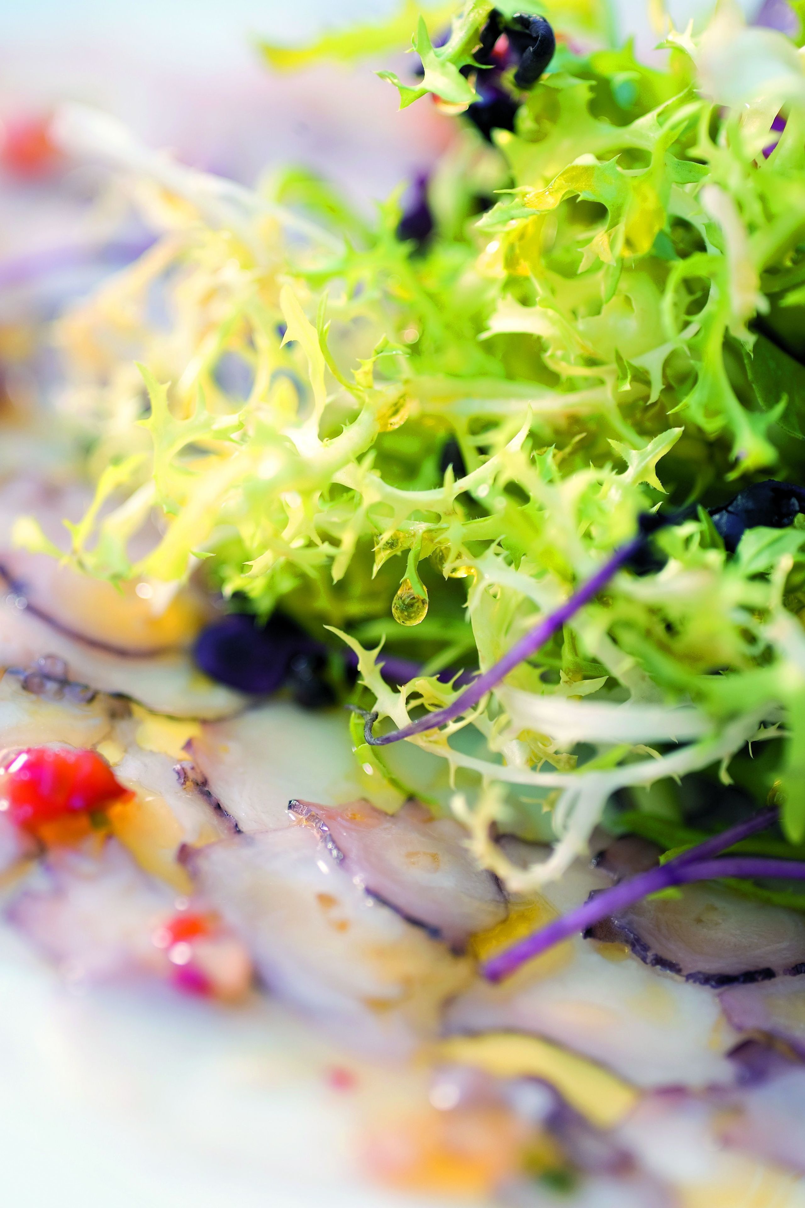 A close-up of a salad with various greens and purple elements.