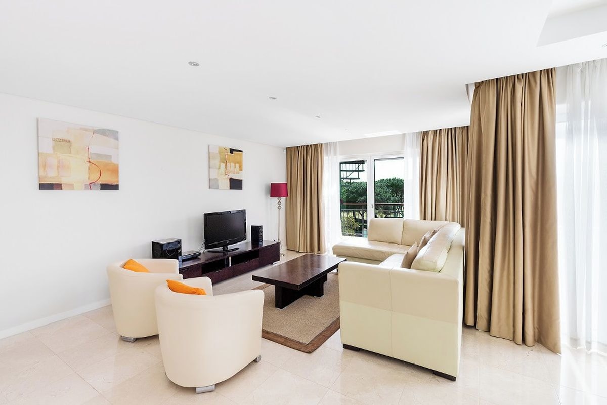 A modern living room with a flat-screen TV, two sofas, a coffee table, and a large window with curtains.