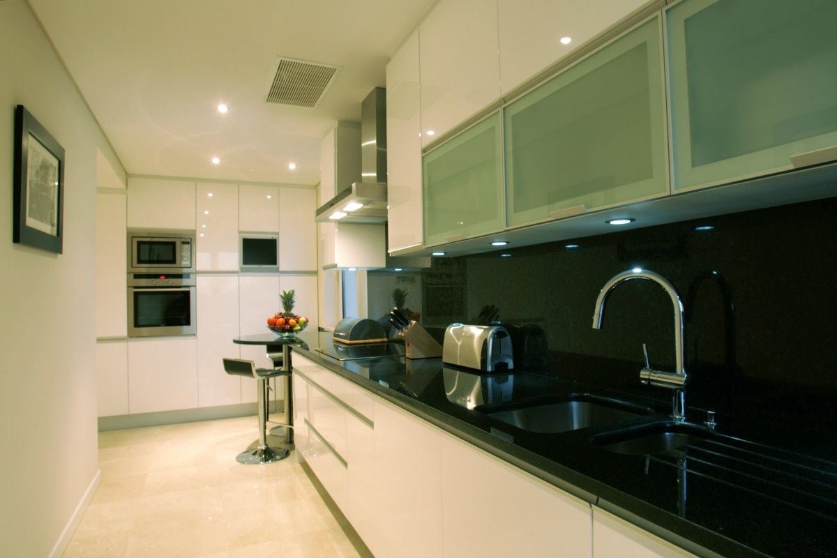Una cocina moderna con encimera negra, pileta de acero inoxidable y microondas.