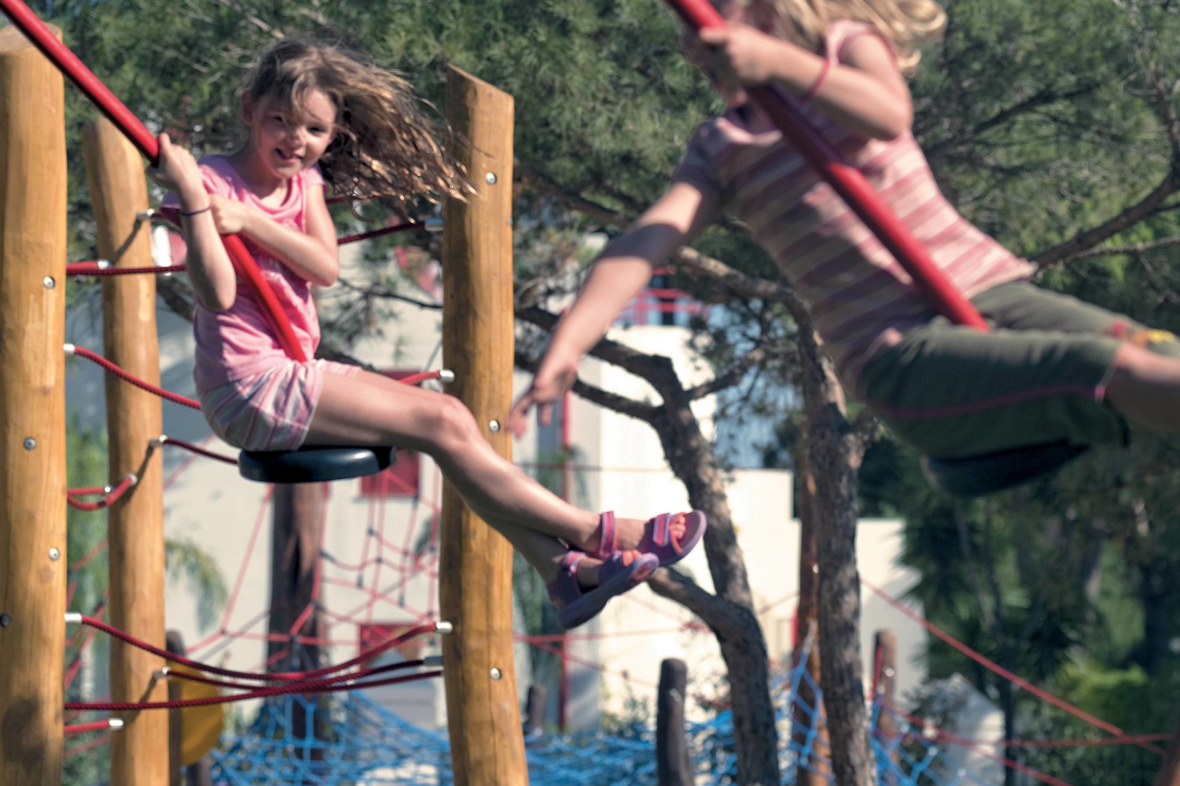 Children playing on a rope bridge in an outdoor setting.