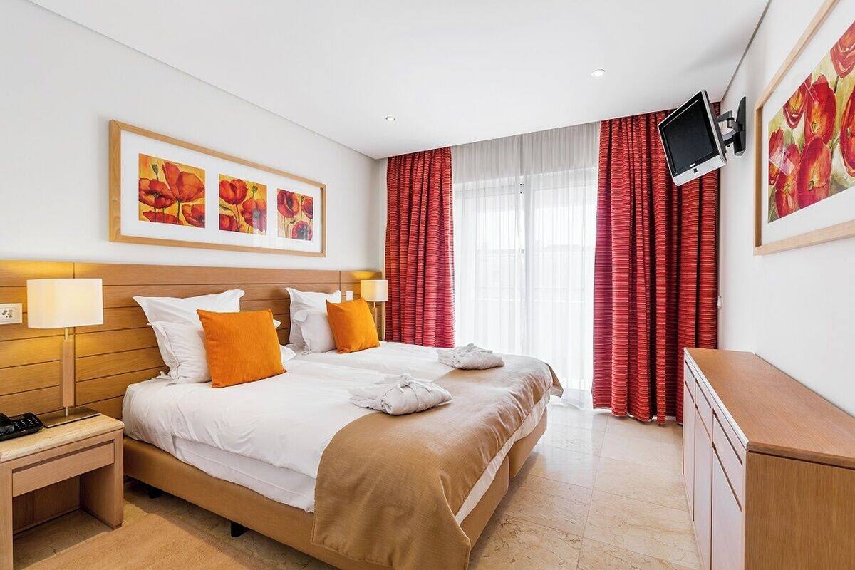 A hotel room with a bed, bedside lamps, a TV, and artwork on the walls.