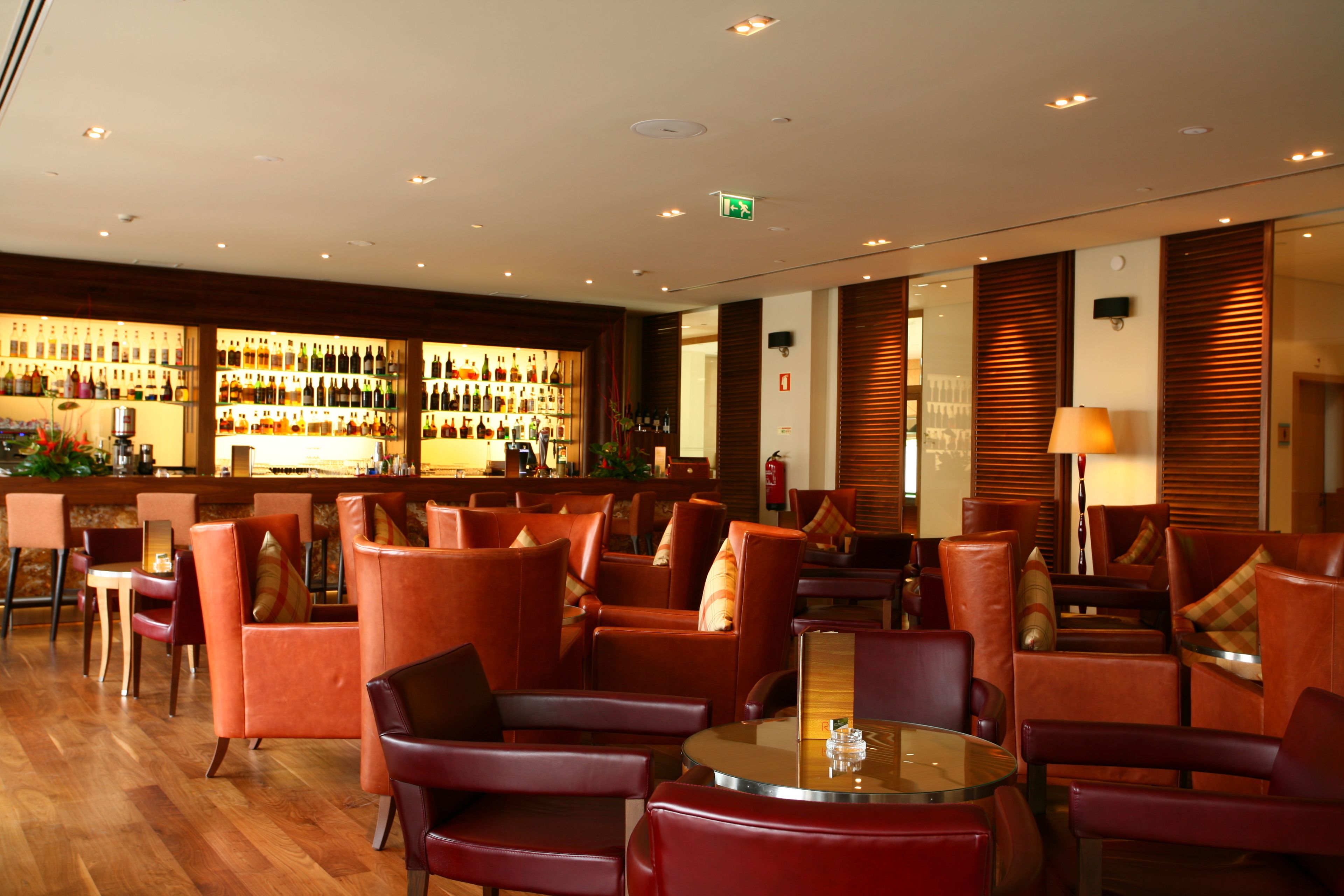 Um saguão de hotel com poltronas de couro, área de bar com garrafas e piso de madeira.