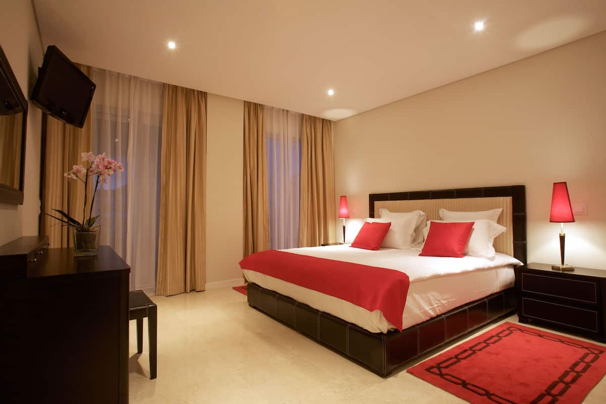 A hotel room with a large bed, two bedside lamps, a TV mounted on the wall, and a desk with a chair.