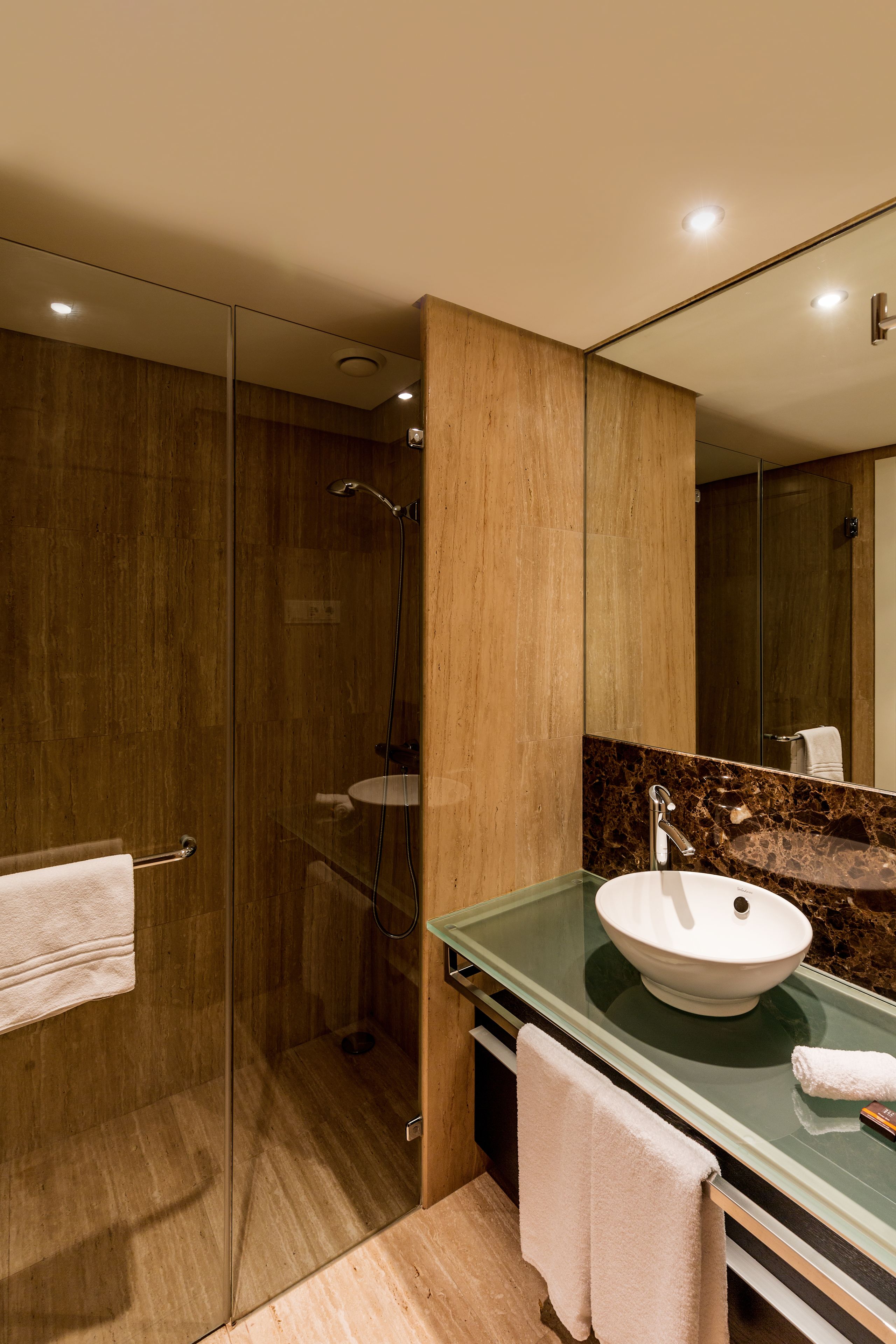 Un baño moderno con ducha de vidrio, encimera de mármol y un espejo grande.