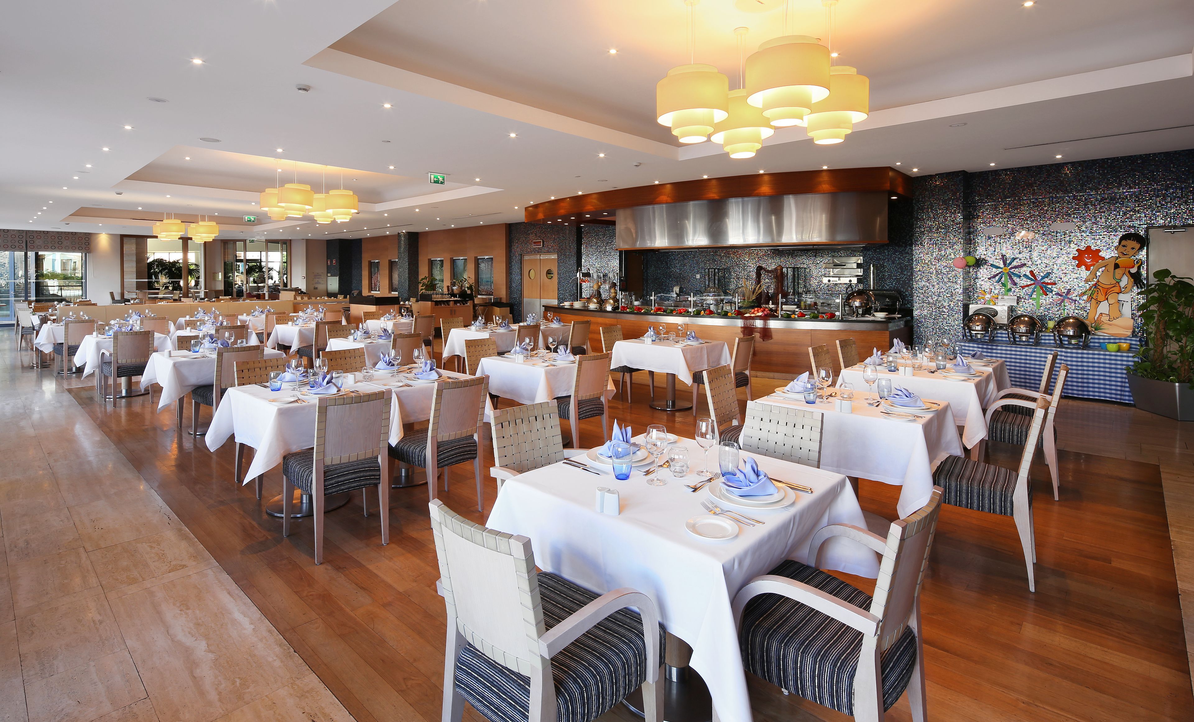 Ein Restaurant mit mehreren Tischen, einer Bar und einer im Hintergrund sichtbaren Küche.
