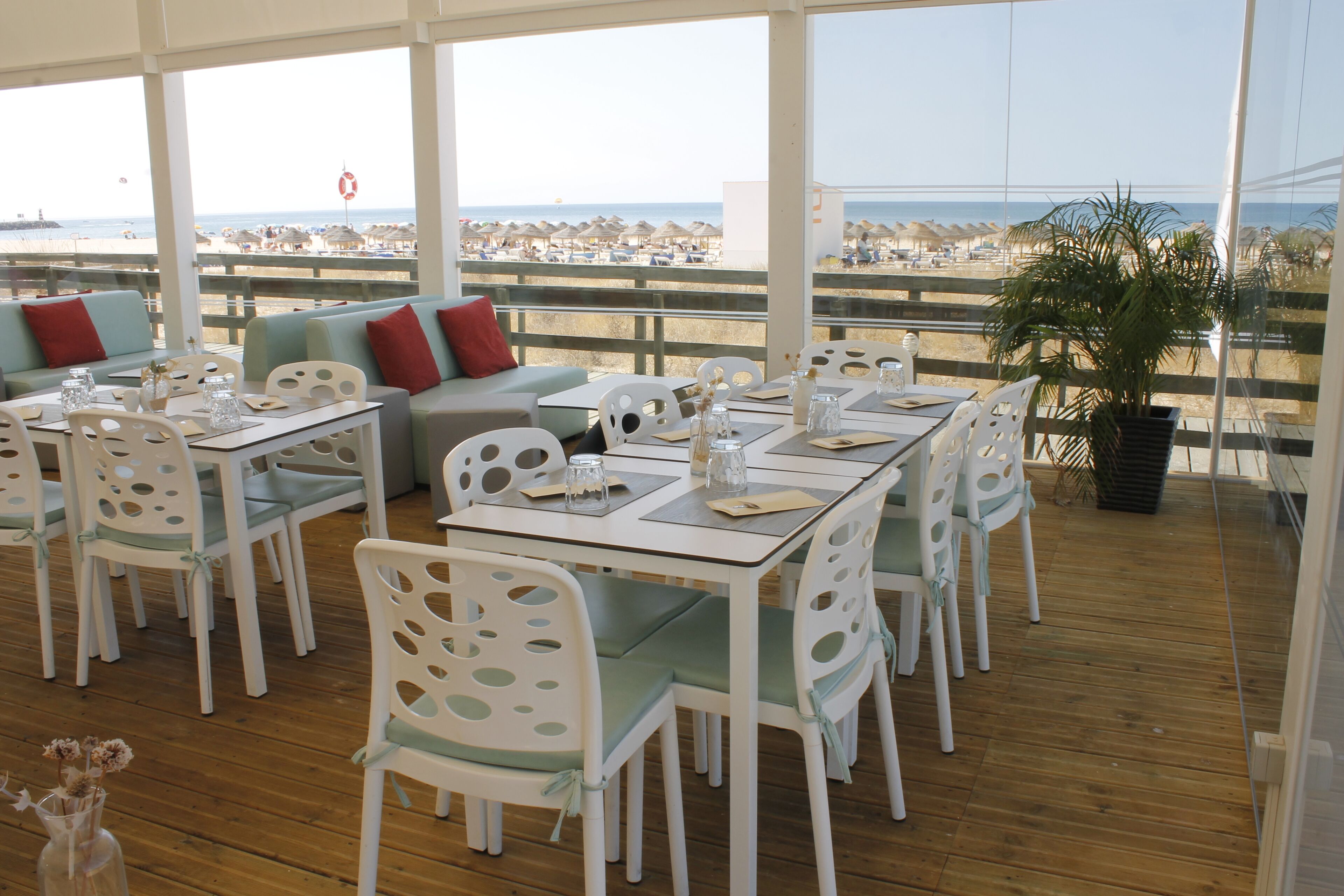 A restaurant with white furniture, a wooden floor, and a view of the beach.