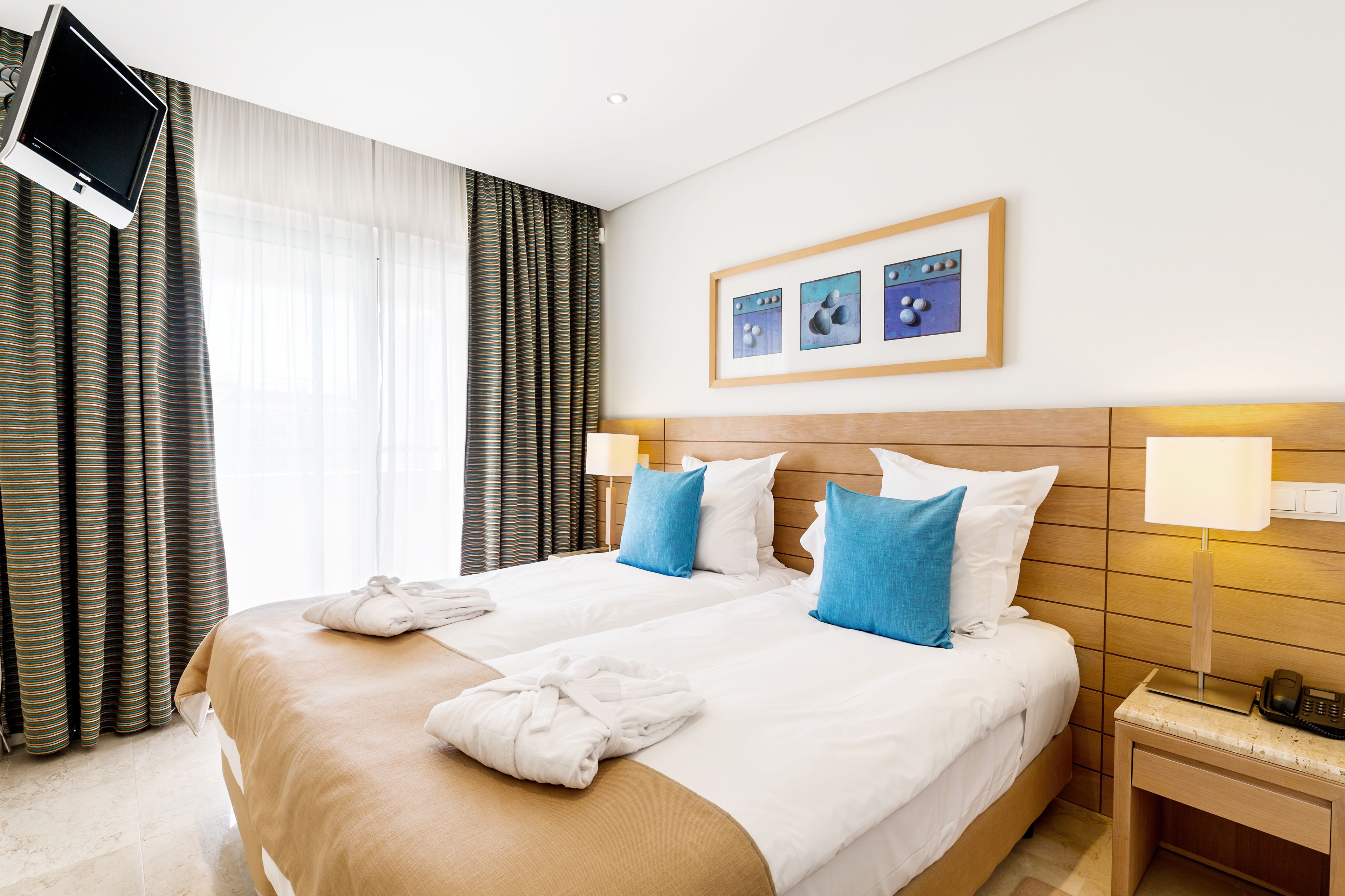 A hotel room with a large bed, two pillows, a TV mounted on the wall, and a framed picture above the bed.