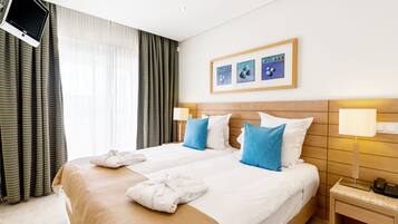 Une chambre d’hôtel avec un grand lit, deux oreillers, un téléviseur fixé au mur et un tableau encadré au-dessus du lit.