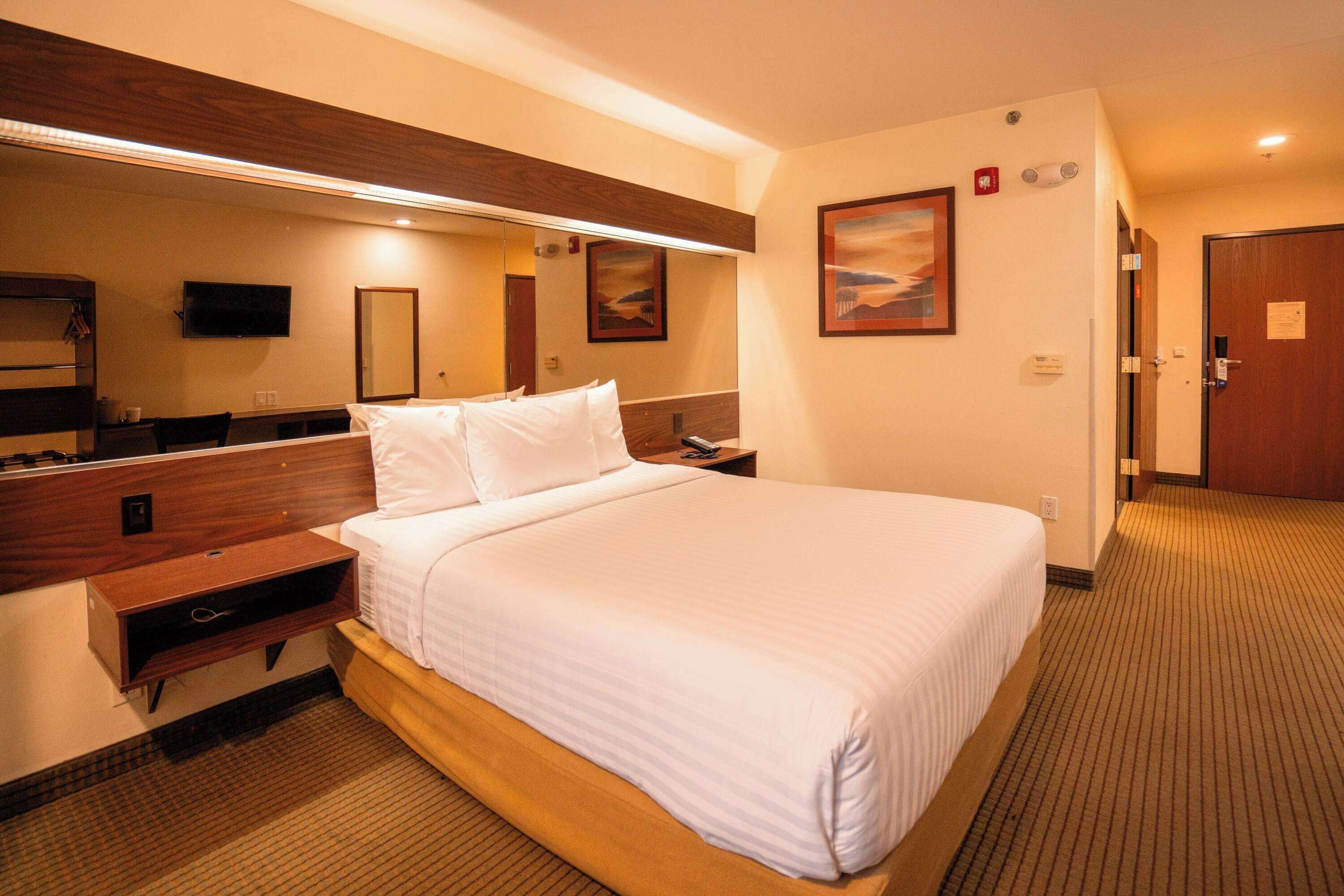 A hotel room with a large bed, a wooden headboard, a flat-screen TV, a bedside table, and a mirror.