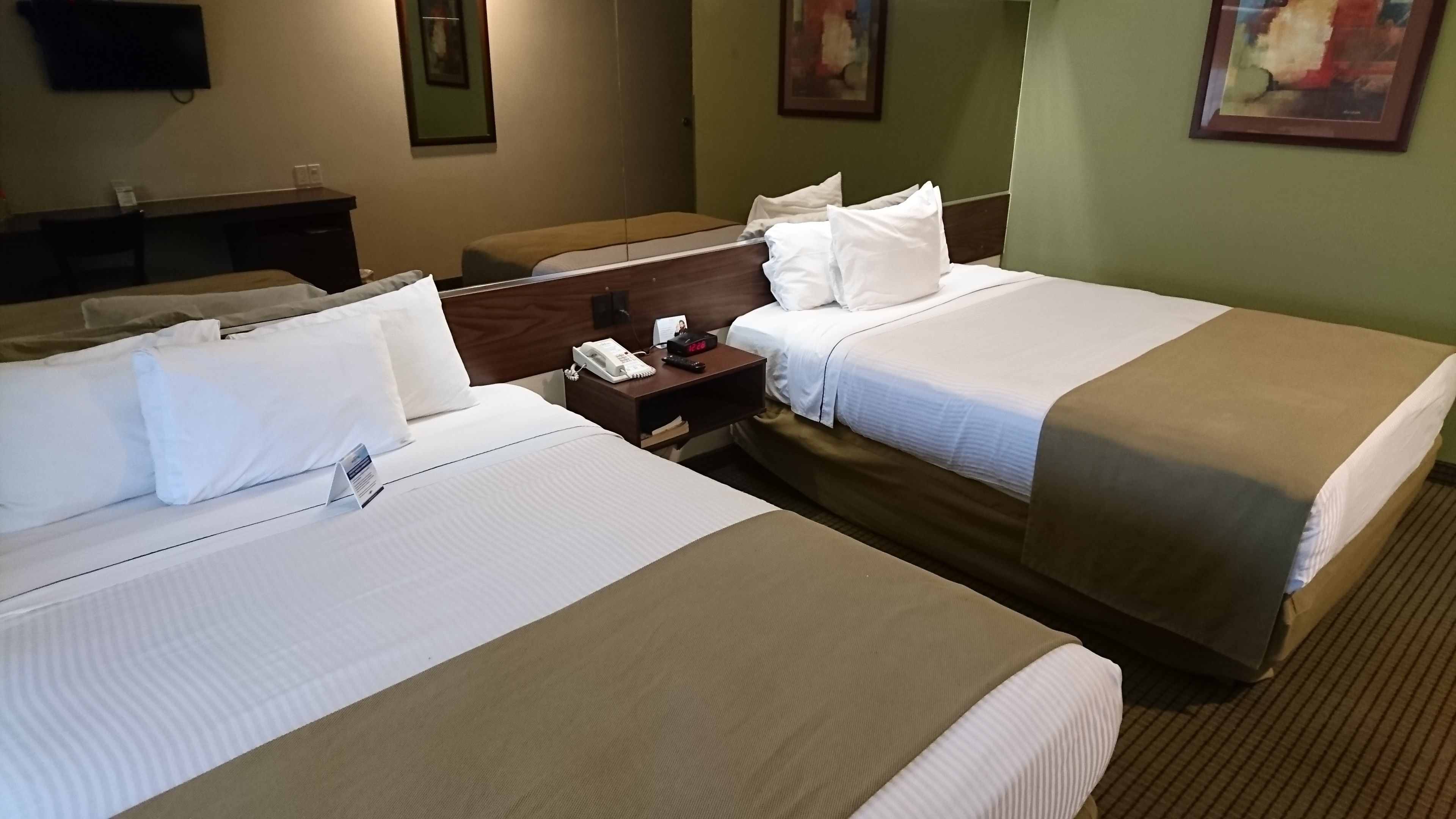 Habitación de hotel con dos camas, una mesita de noche con un teléfono y un mando a distancia, y un escritorio con una silla.