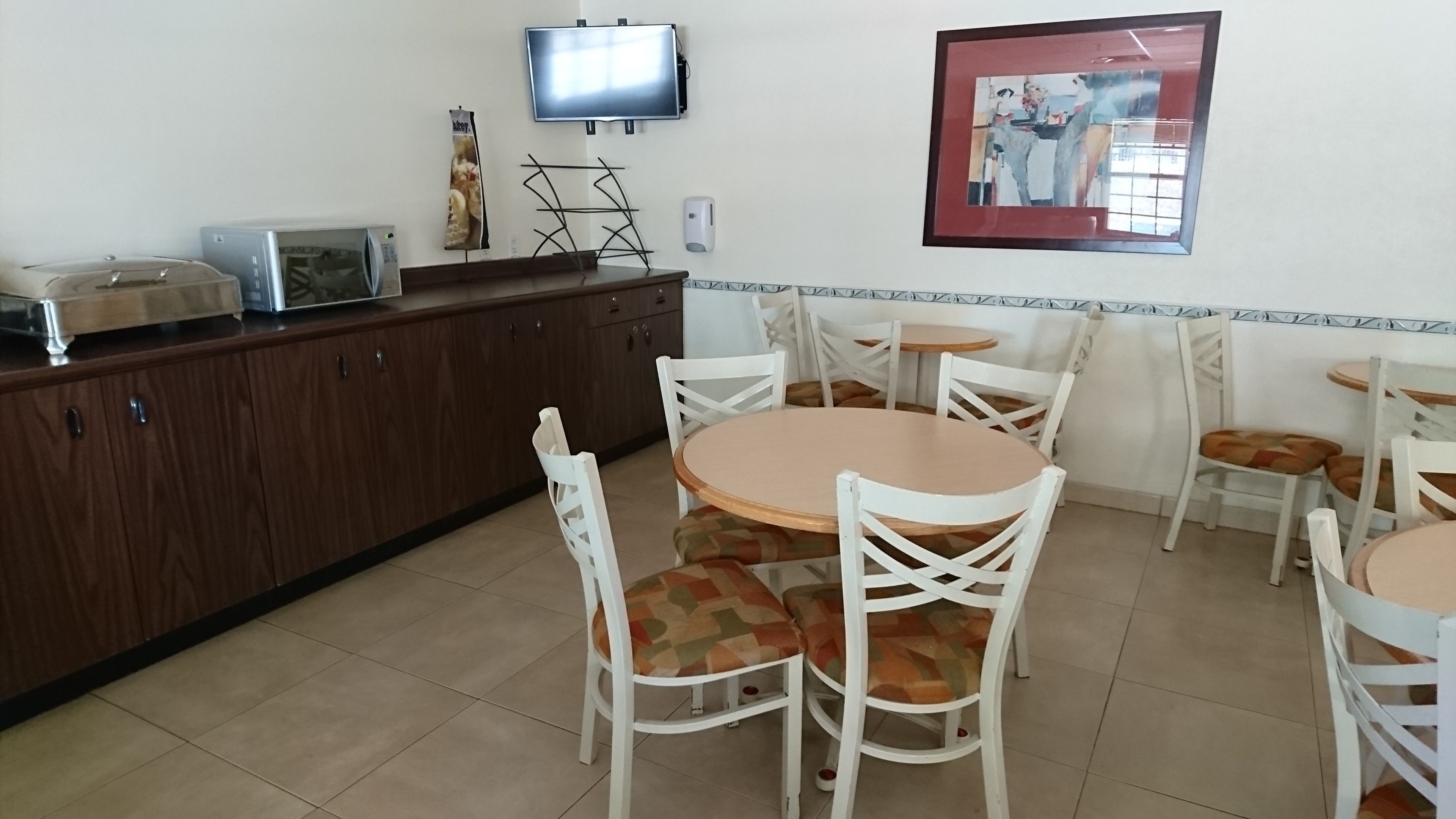 Un comedor con mesas redondas y sillas blancas, un televisor montado en la pared y un cuadro colgado sobre las mesas.