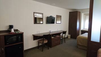 A hotel room with a kitchenette, a desk with two chairs, a bed, a TV mounted on the wall, and a window.