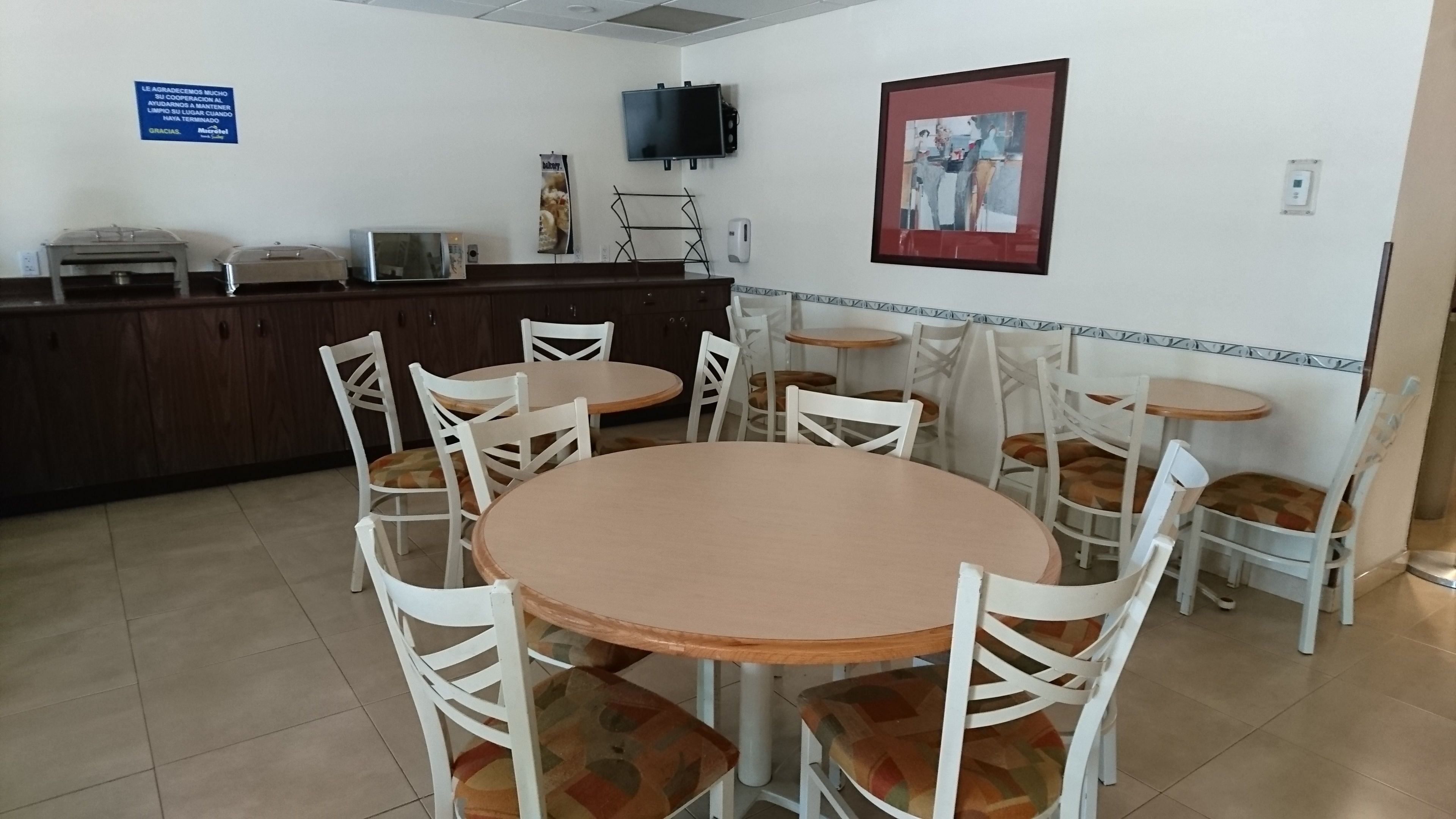 Un comedor con una mesa redonda y sillas, una encimera con microondas y un televisor montado en la pared.