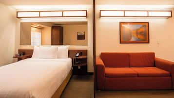 A hotel room with a bed, a nightstand, a red sofa, a painting, and a mirror.