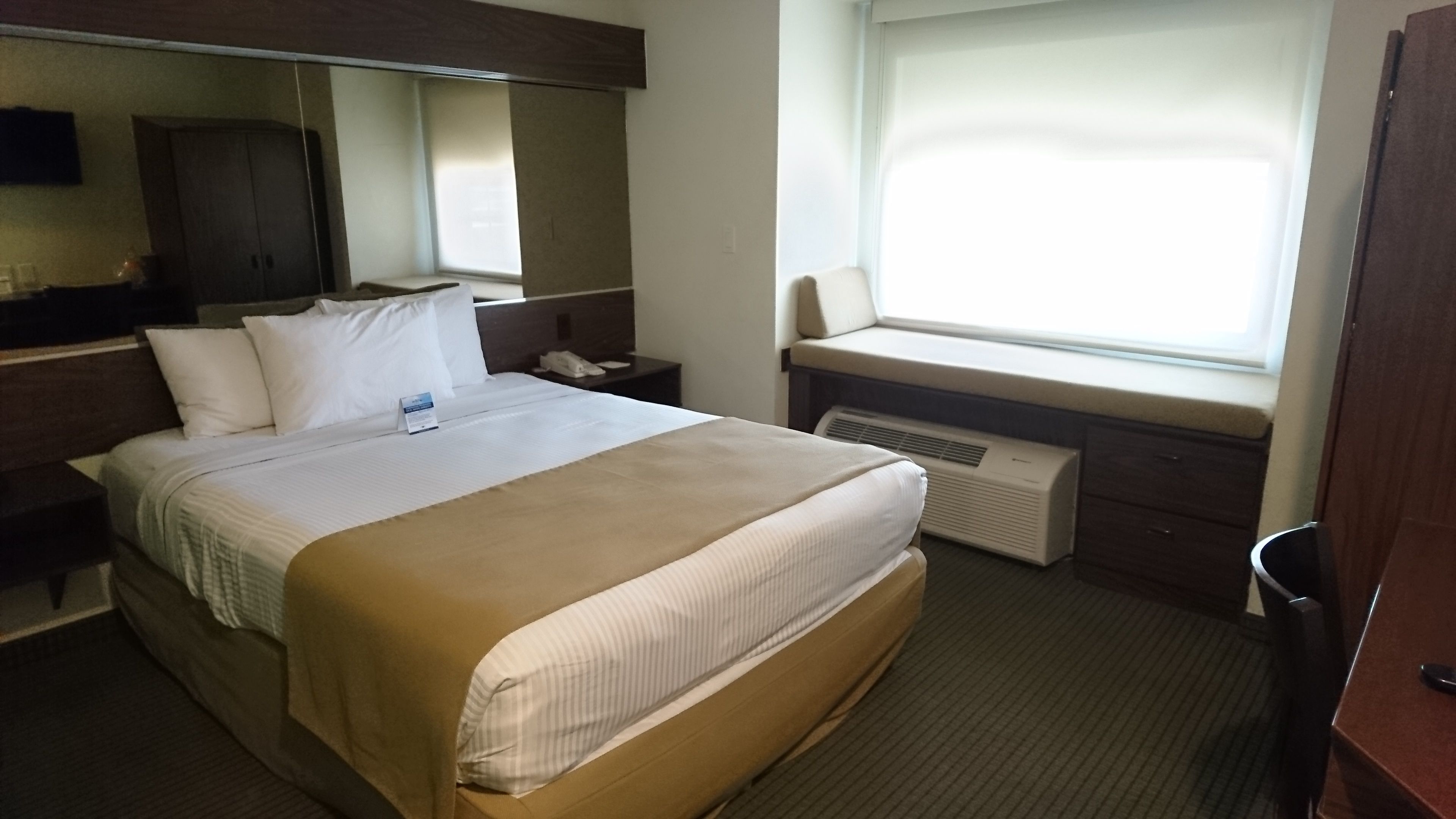 Une chambre d’hôtel avec un grand lit, une table de chevet avec un téléphone, une fenêtre donnant sur un beau paysage et un miroir au mur.