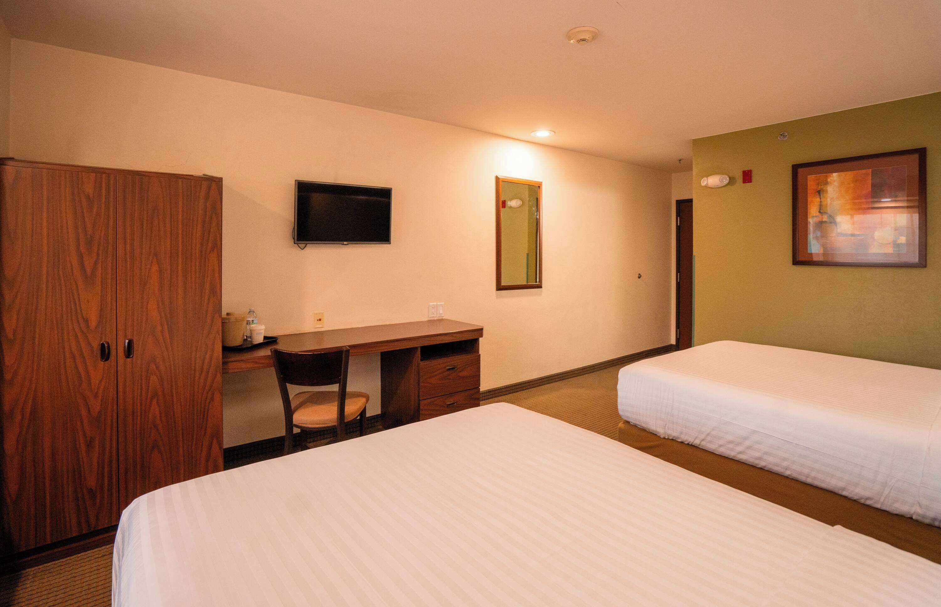 Een hotelkamer met twee bedden, een houten garderobe, een bureau met stoel, een televisie, een spiegel en een lijst met een afbeelding aan de muur.