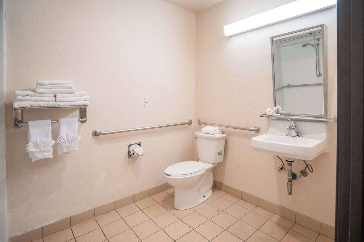 Un baño con inodoro, lavamanos y barras de apoyo.