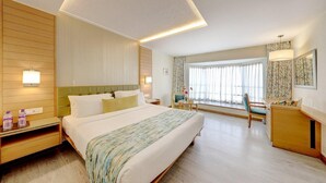 Una habitación de hotel con una cama grande, mesitas de noche, un escritorio y una ventana con cortinas.