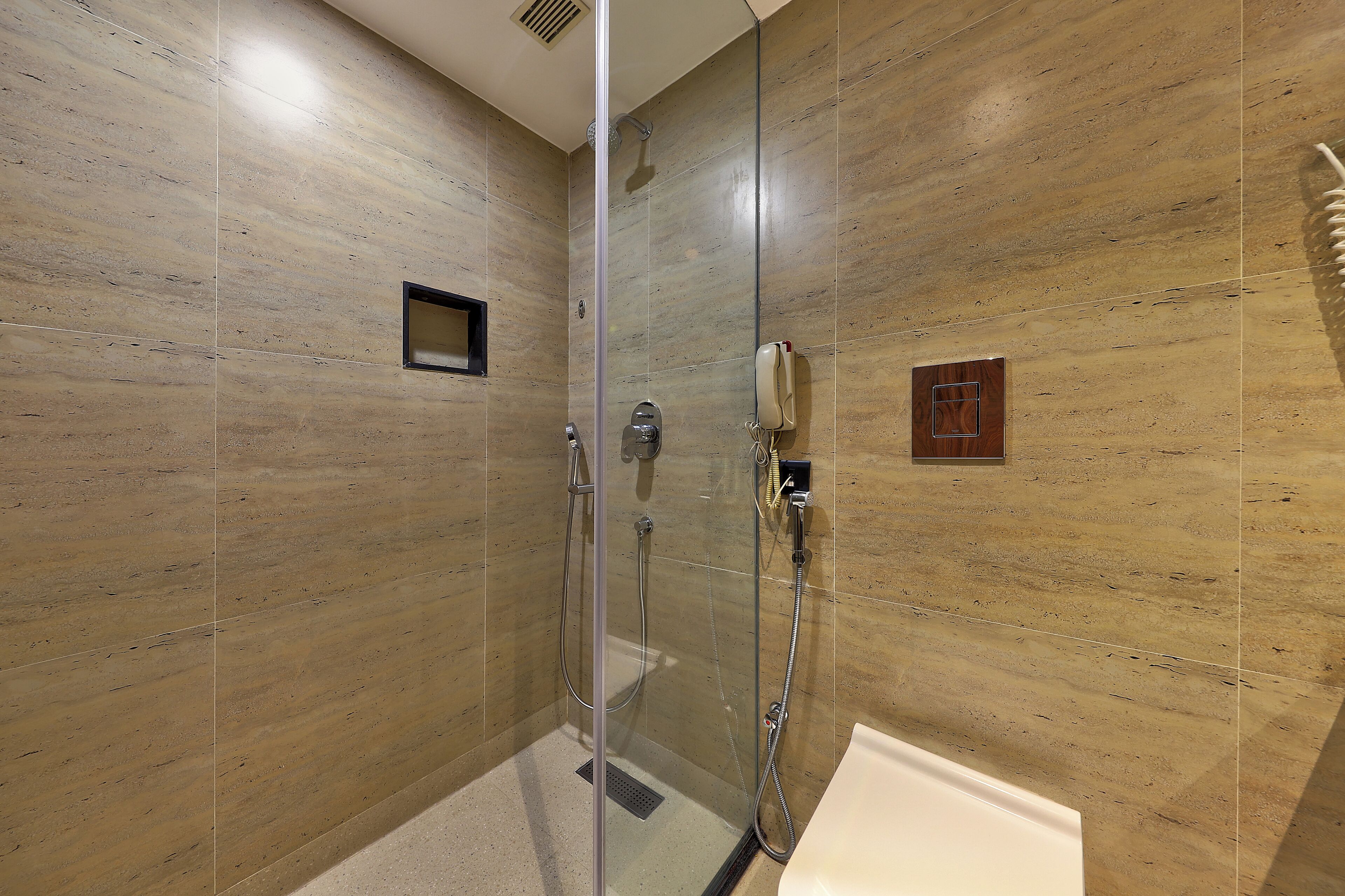 Un baño moderno con ducha de vidrio, una bañera blanca y un revestimiento de mármol en la pared.