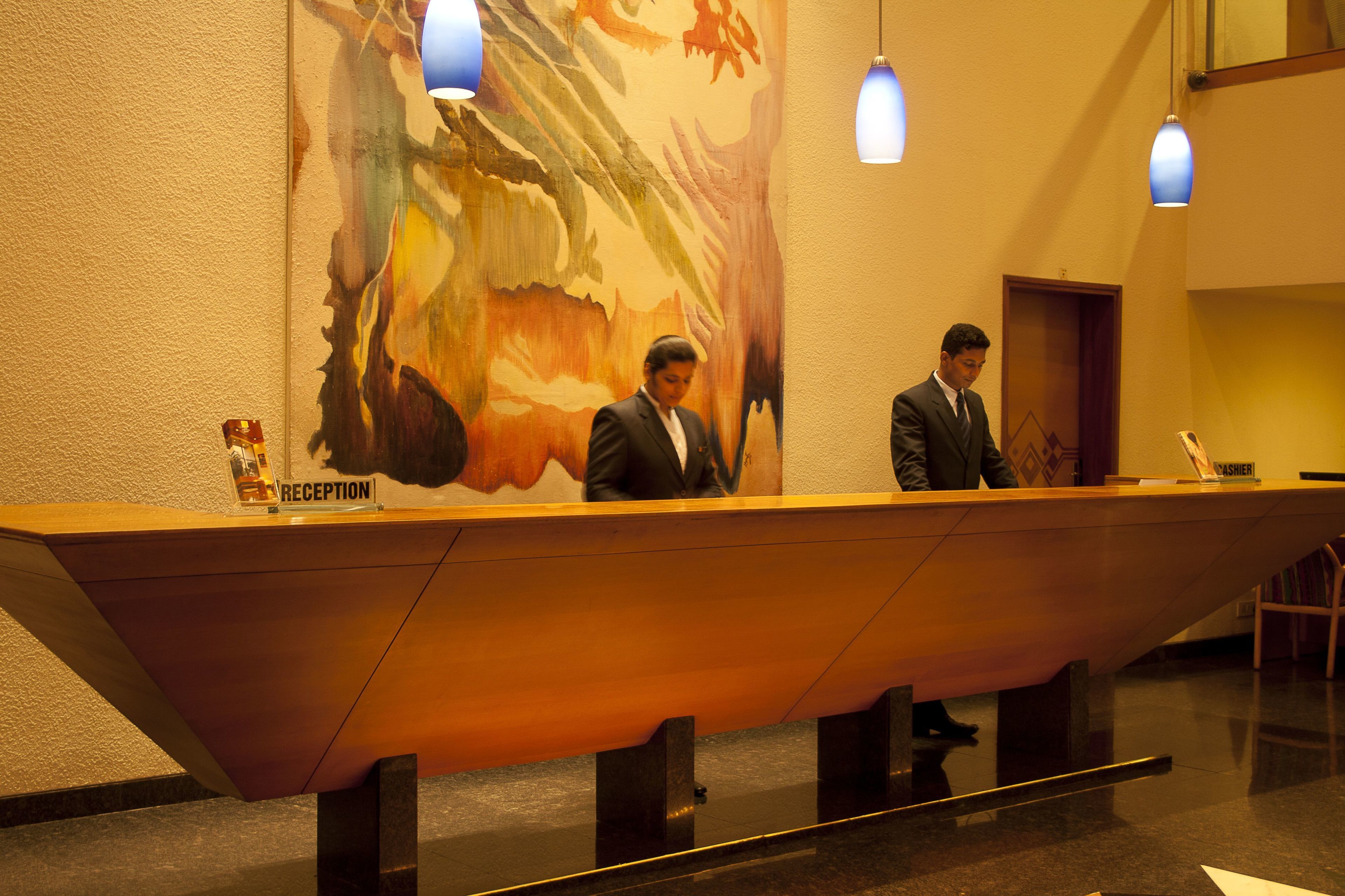 Un mostrador de recepción en el vestíbulo de un hotel, con un gran mural abstracto en la pared de fondo.