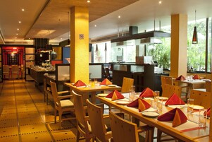 Un restaurante con mesas y sillas de madera, servilletas rojas y piso de baldosas.