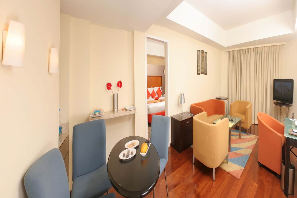 Habitación de hotel con cama, televisor, escritorio, silla, mesita y sofá.