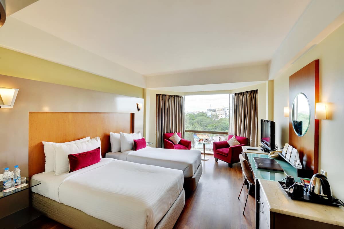 A hotel room with two beds, a desk, a TV, and a view of the city.