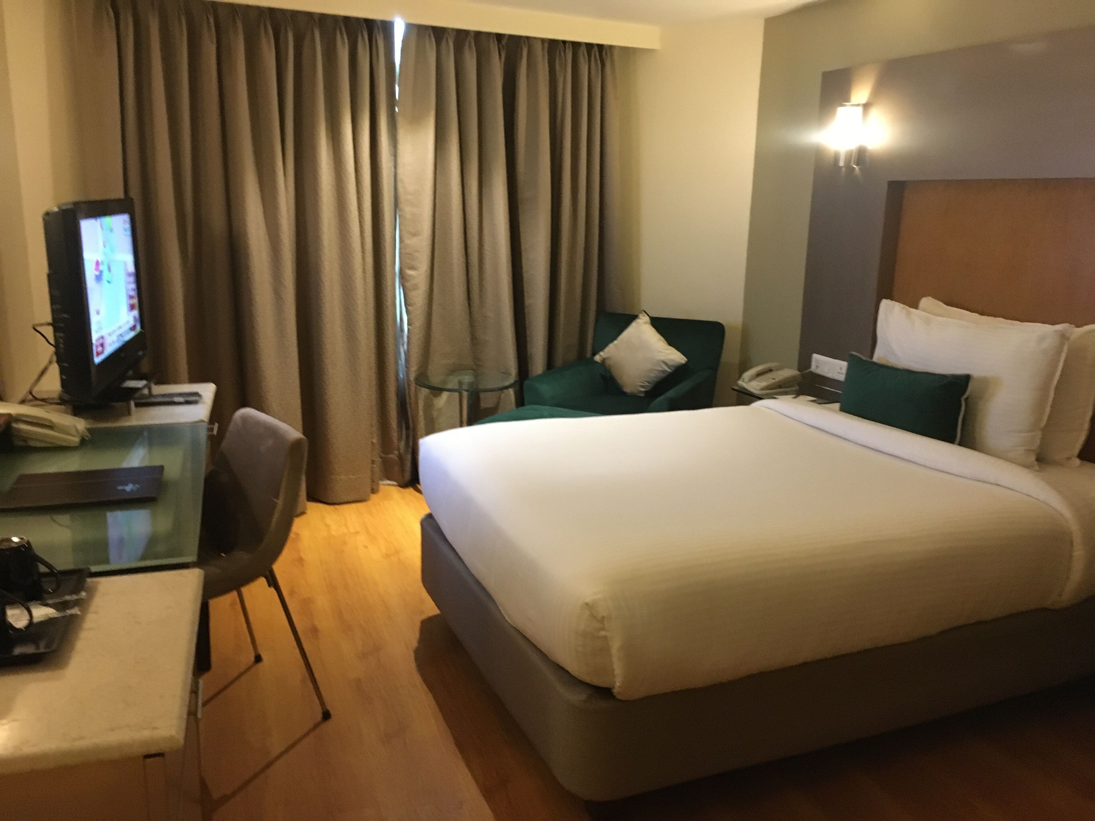 Habitación de hotel con cama, escritorio con computadora, silla, mesita y teléfono.