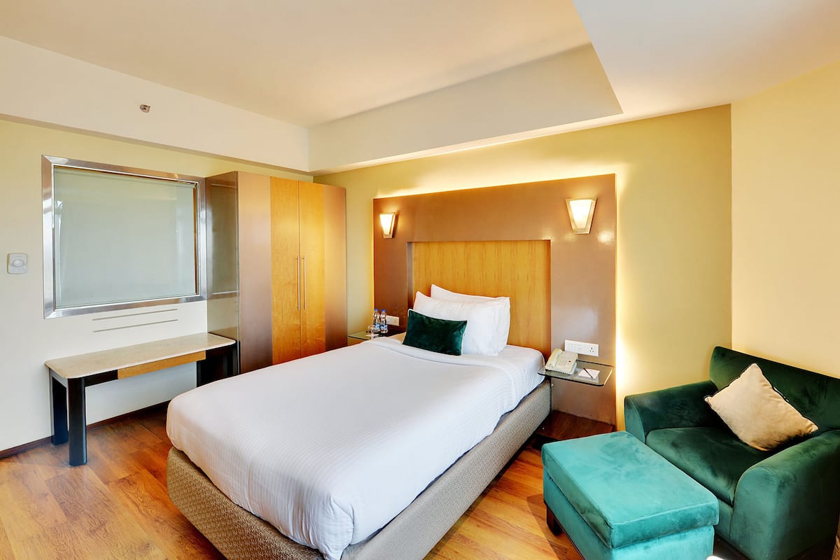 Habitación de hotel con una cama grande, un escritorio, un armario, un sillón verde y un televisor de pared.