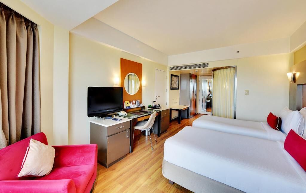 A hotel room with a bed, a desk with a computer, a TV, and a red couch.