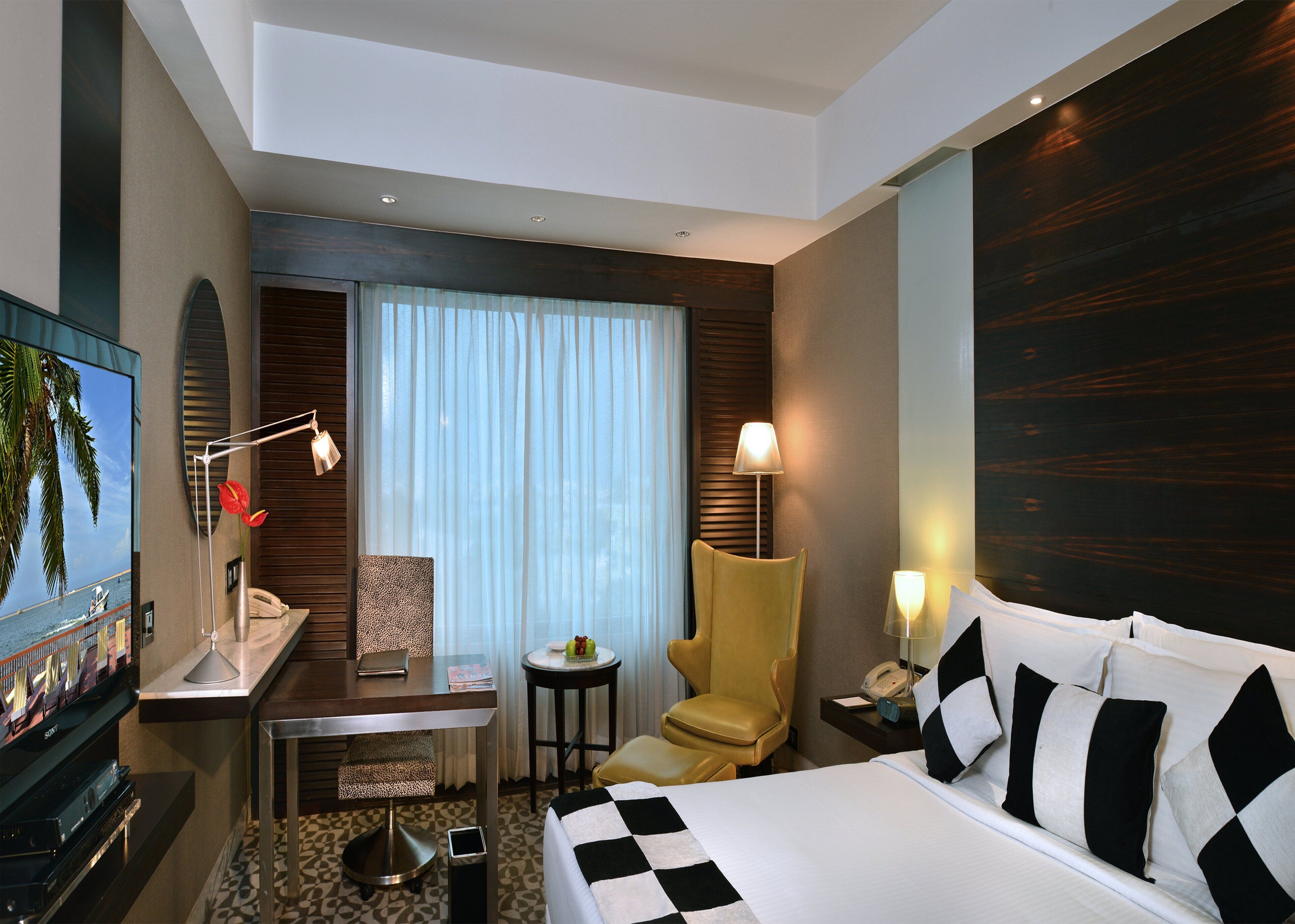 Ein Hotelzimmer mit Bett, Schreibtisch, Stuhl, Fernseher und einem fensterbepflanzten Fenster.