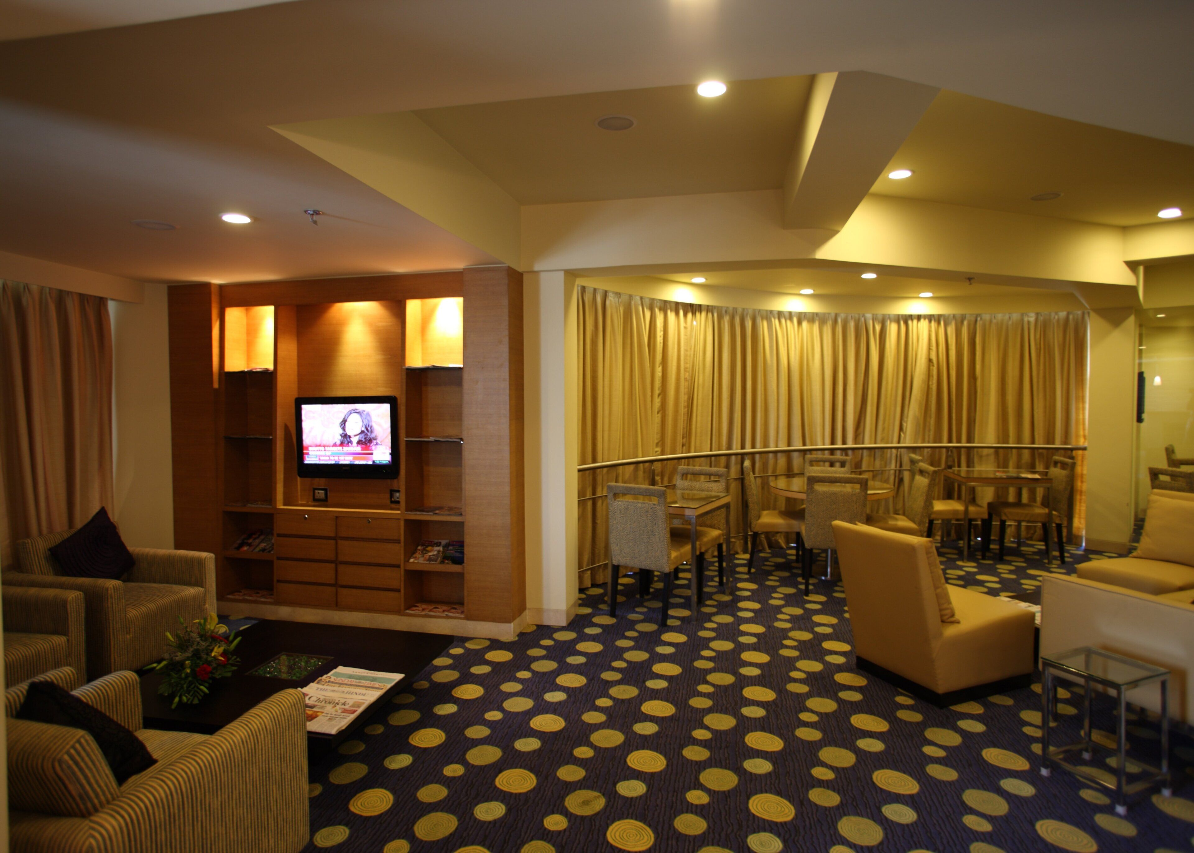 A hotel lobby with a TV, seating area, and a patterned carpet.