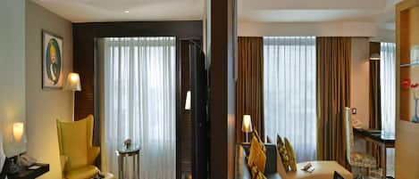 A hotel room with a bed, a sofa, a desk with a laptop, a chair, a small table with a lamp, and a staircase.